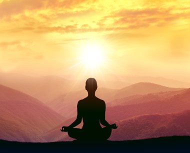 Dağlarda yoga yapan bir kadının silüeti.