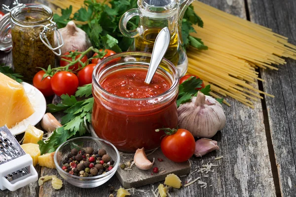 Molho de tomate em um frasco de vidro e ingredientes em fundo de madeira — Fotografia de Stock