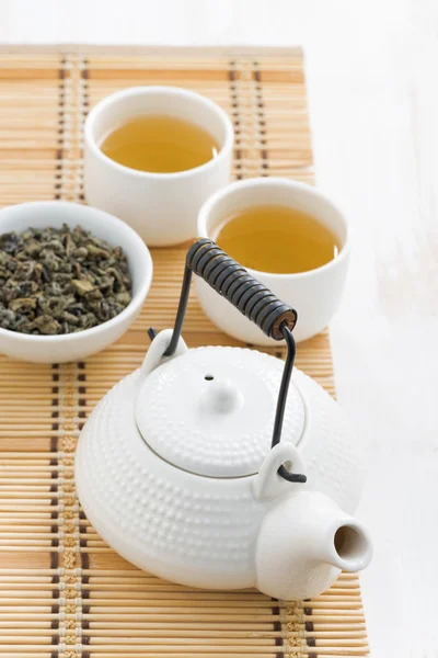 Theepot en kopjes groene thee op een rieten mat, bovenaanzicht — Stockfoto