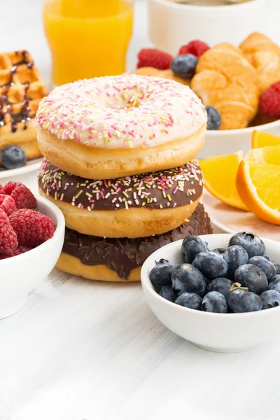 Glasierte Donuts, Süßigkeiten und frische Beeren auf weißem Tisch, senkrecht — Stockfoto