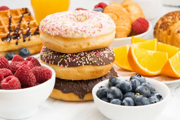 Rosquillas glaseadas, dulces y bayas frescas sobre una mesa blanca — Foto de Stock