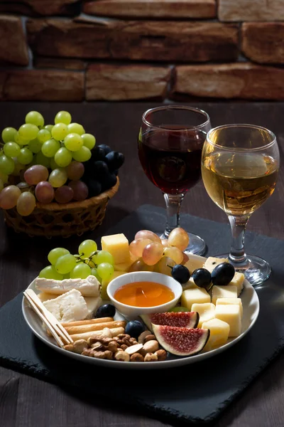 Plate with deli snacks and wine on a dark background, vertical — Stock Photo, Image