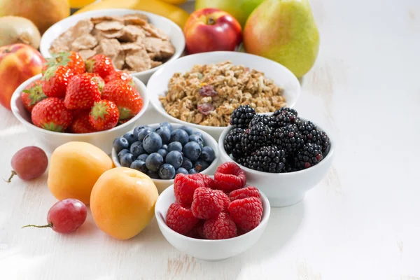 Bayas frescas, fruta y muesli para el desayuno en la mesa blanca —  Fotos de Stock