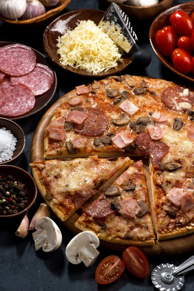 Pizza med salami och ingredienser på svart bakgrund, vertikal — Stockfoto