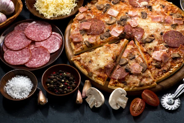 Pizza med salami och ingredienser på en svart bakgrund, närbild — Stockfoto