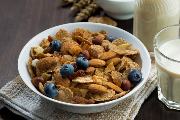 breakfast cereal flakes with blueberries and nuts on dark table