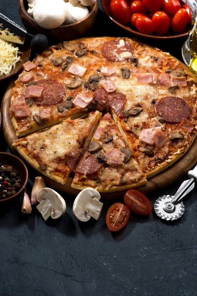 Pizza med salami och ingredienser på en mörk bakgrund, vertikal — Stockfoto