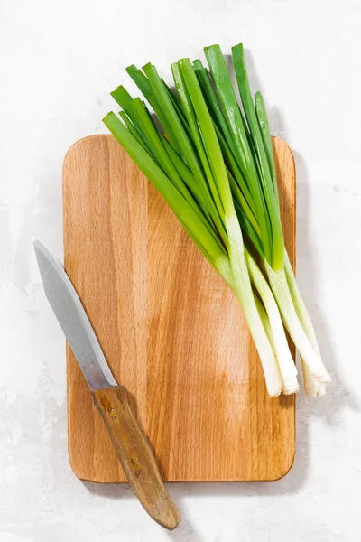 Wooden cutting board and green onions, vertical top view — Stock Photo, Image