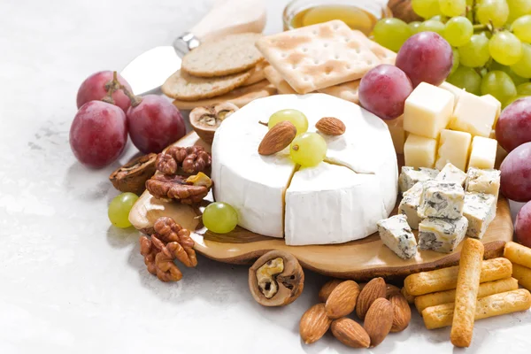 Camembert, uvas e lanches em uma mesa branca, close-up — Fotografia de Stock