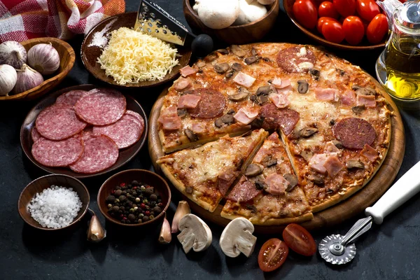 Pizza med salami och ingredienser på en mörk bakgrund, ovanifrån — Stockfoto