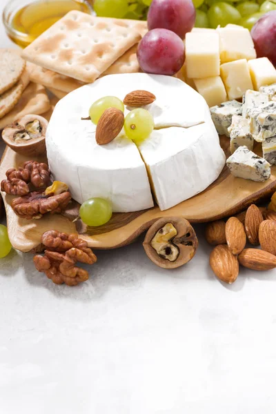 Camembert, Trauben und Snacks auf einem weißen Tisch, senkrecht — Stockfoto