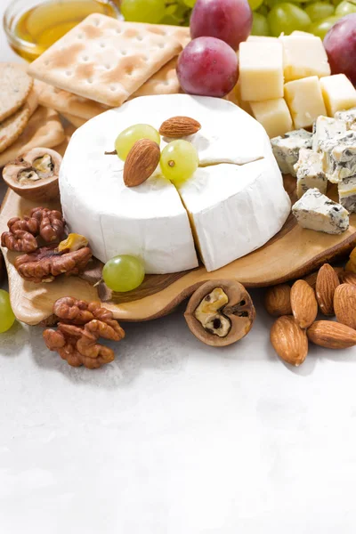 Camembert, uvas y aperitivos sobre una mesa blanca, vertical — Foto de Stock