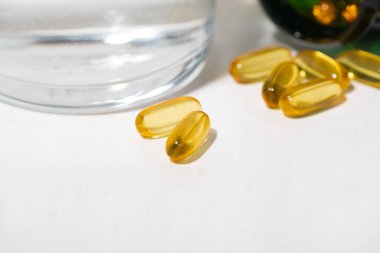 Beslenme takviyesi - balık yağı kapsülleri ve bir bardak su, yakın plan.