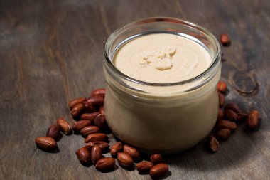 Ahşap bir arka planda cam kavanozda fıstık ezmesi, yatay.