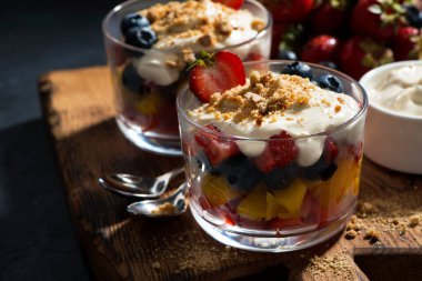 Tahta bir tahtanın üzerinde muhallebi kaplı çeşitli taze meyveler, yatay ve yakın plan.