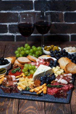Çeşitli peynirler, meyve ve etler ahşap masada şarap, dikey