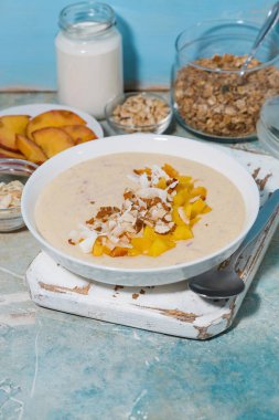 Kahvaltıda mangolu, hindistan cevizli ve fındıklı sağlıklı meyve suyu kasesi.