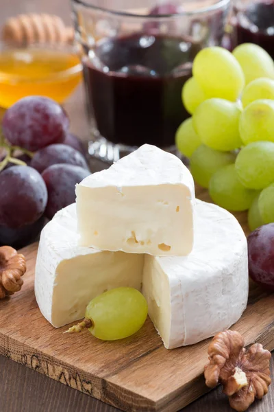 Fresh camembert on a wooden board and grapes, vertical — Stock Photo, Image