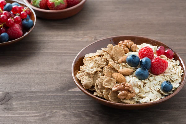 Harina de avena y muesli en un tazón, bayas frescas en la mesa de madera — Foto de Stock