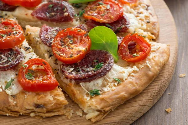 Pizza deliciosa com salame e tomate em uma tábua de madeira — Fotografia de Stock