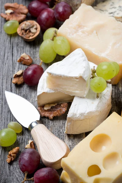 Assortment of cheeses, grapes and walnuts on a wooden background — Stock Photo, Image