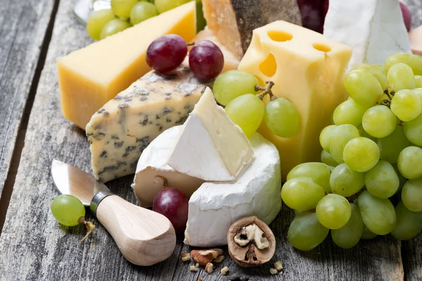 Assortment of fresh cheeses and grapes on a wooden background — Stock Photo, Image