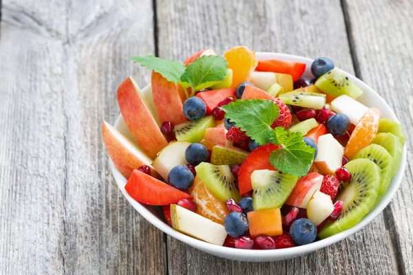 Insalata di frutta e bacche in una ciotola su uno sfondo di legno, primo piano — Foto Stock