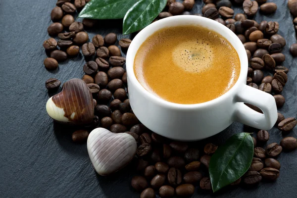 Taza de café expreso sobre granos de café fondo y caramelos de chocolate —  Fotos de Stock