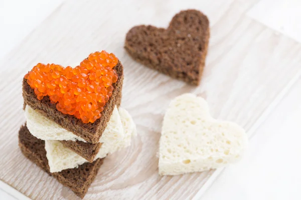 Toasts with red caviar in heart shape on wooden board — Stock Photo, Image
