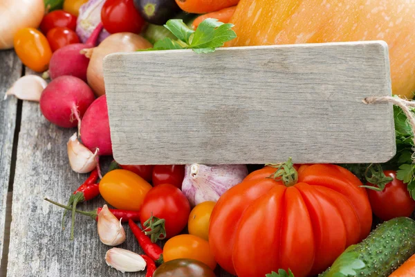 Surtido de verduras frescas de temporada y una placa de madera — Foto de Stock