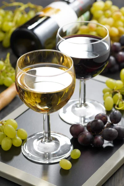 Vinho branco e tinto em copos, uvas no fundo — Fotografia de Stock