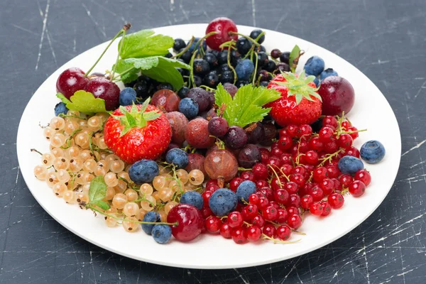 Sortierte Gartenbeeren auf einem Teller auf dunklem Hintergrund — Stockfoto