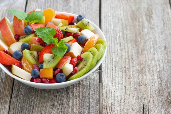 Insalata di frutta e bacche in una ciotola su uno sfondo di legno — Foto Stock