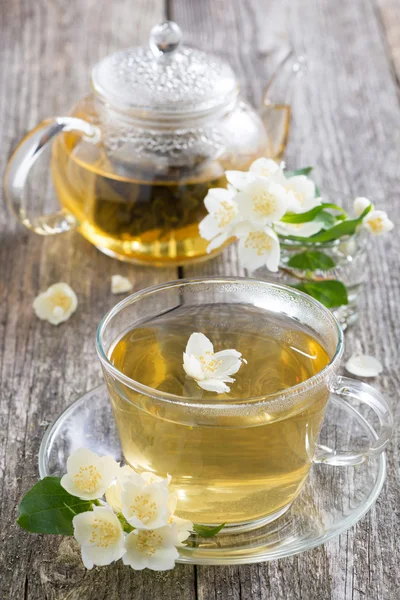 Kettle and a cup of green tea with jasmine on wooden table — Stock Photo, Image