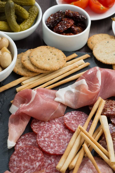 Assorted meat snacks, sausages and pickles on a blackboard, top — Stock Photo, Image