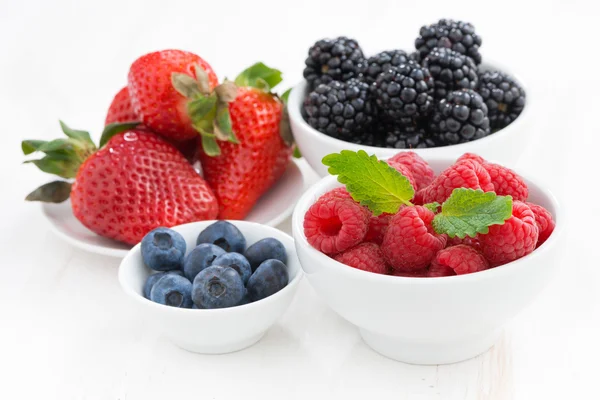 Frische Beeren in Schalen auf einem weißen Holztisch — Stockfoto