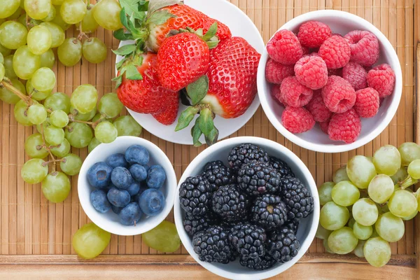 Свежие ягоды в миске и зеленый виноград на деревянном подносе, сверху соперничество — стоковое фото