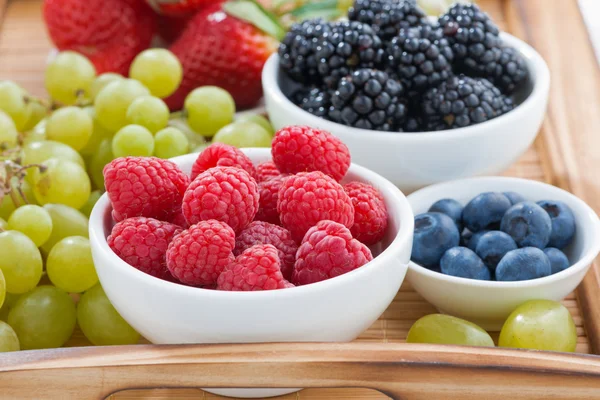 Tazón de frambuesas, bayas frescas y uvas verdes en una madera — Foto de Stock