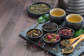 assortment of fragrant dried teas and green tea on dark wooden t