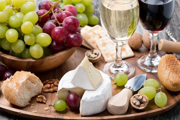 Камембер, свежий багет, виноград, грецкие орехи и вино на деревянной тарелке — стоковое фото
