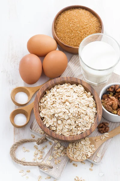 Fiocchi d'avena e ingredienti su un tavolo di legno bianco, verticale, a — Foto Stock