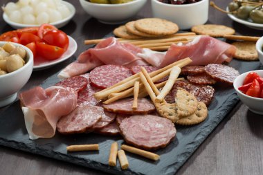 Çeşitli et aperatifler, sosis ve bir kara tahta üzerinde turşu