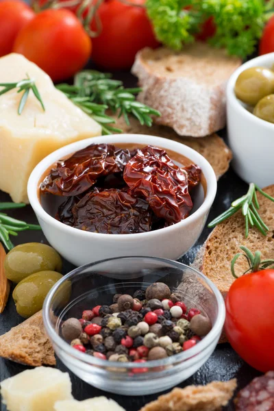 Sonnengetrocknete Tomaten in einer Schüssel und verschiedene Vorspeisen, senkrecht — Stockfoto