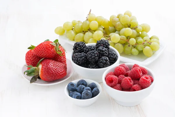 Frische Gartenbeeren und Weintrauben auf einem weißen Holztisch — Stockfoto