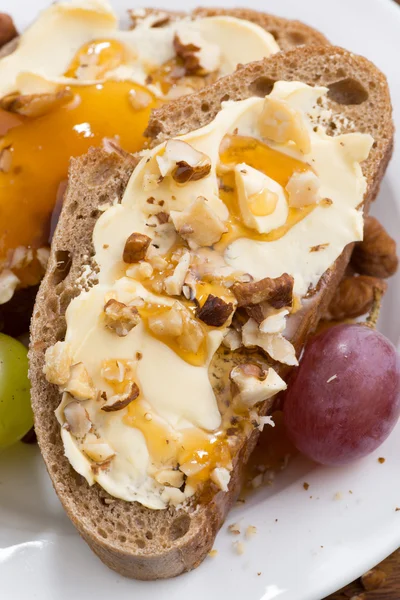 Bread with butter, honey, nuts and grapes, vertical, close-up — Stock Photo, Image