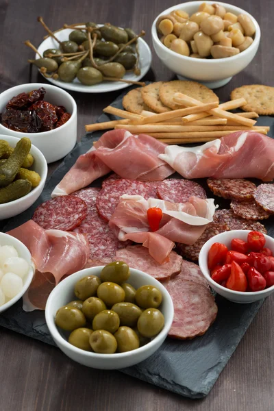 Snack di carne Deli, salsicce e sottaceti su un tavolo di legno scuro — Foto Stock