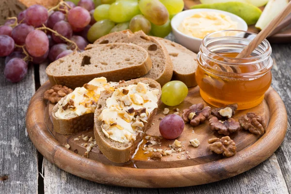 Bread with butter, honey, nuts and grapes on wooden board — Stock Photo, Image