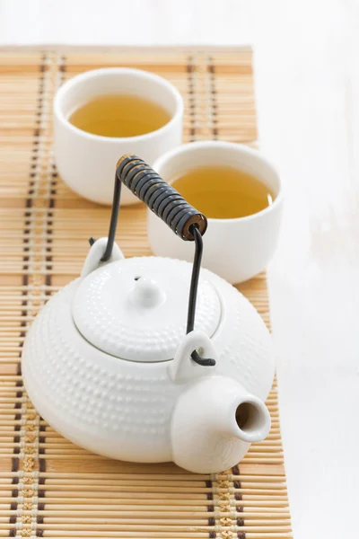 Teapot and cups of green tea on a wicker mat — Stock Photo, Image