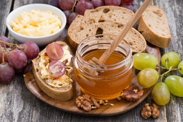 Flavored honey, bread with butter and grape on wooden board — Stock Photo, Image