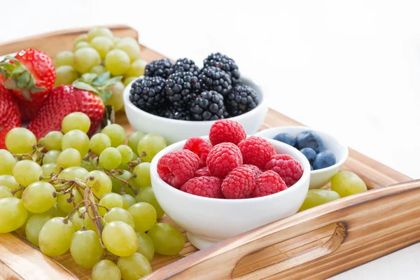 Bandeja de madera con bayas frescas y uvas sobre mesa blanca — Foto de Stock